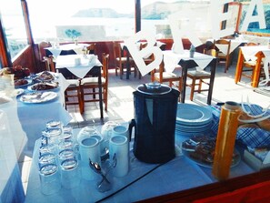 Un área de comedor al aire libre con mesas dispuestas para una comida, incluyendo platos, cubiertos y una cafetera.