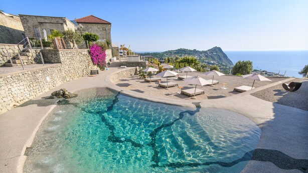 A pool area with clear water, surrounded by lounge chairs and umbrellas, overlooking a scenic coastal view. - Tenuta C'est la Vie (Forio)