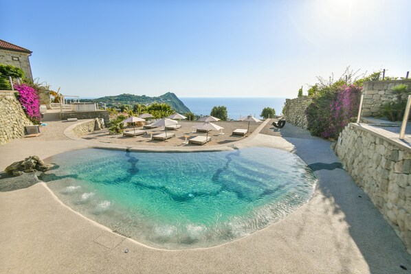 A pool area with a clear view of the sea, stone walls, and outdoor seating. - Tenuta C'est la Vie (Forio)