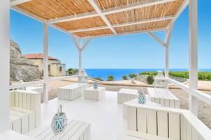 Un espacio de estar al aire libre con techo, mobiliario blanco y vista al mar.