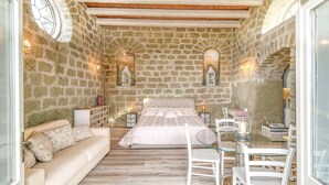 A bedroom with a stone wall, a bed, a sofa, a glass table, and two nightstands with lamps. - Tenuta C'est la Vie (Forio)