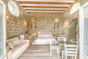 Un dormitorio con pared de piedra, una cama, un sofá, una mesita de vidrio y dos mesitas de noche con lámparas.