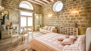 A bedroom with a large bed, a glass dining table, and a sofa. There are two arched windows and a stone wall. - Tenuta C'est la Vie (Forio)