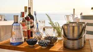 A table with various bottles, glasses, and bowls, likely for a cocktail or aperitif, set against a backdrop of a balcony with a view of the sea. - Tenuta C'est la Vie (Forio)