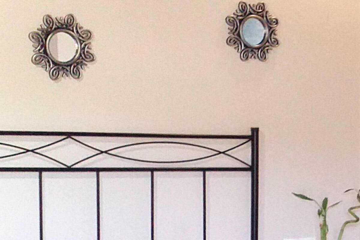 A bed with a patterned pillow, a bedside table with a vase, and two wall mirrors.