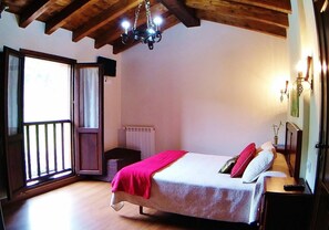 A bedroom with a wooden ceiling, a bed with a red blanket, a nightstand, and a window with a view. - El Rincón de Yaxu (Llanes)