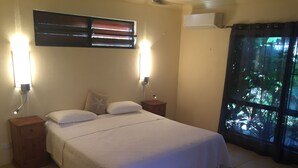 Une chambre à coucher comprenant un lit, deux tables de chevet, un climatiseur fixé au mur et une fenêtre avec des rideaux.