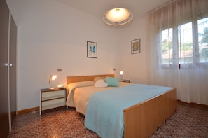 A bedroom with a bed, bedside lamps, a nightstand, and a window with curtains. - Villa Ralph (Lignano Sabbiadoro)