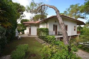 A two-story house with a balcony, surrounded by lush greenery and a well-maintained garden. - Villa Ralph (Lignano Sabbiadoro)