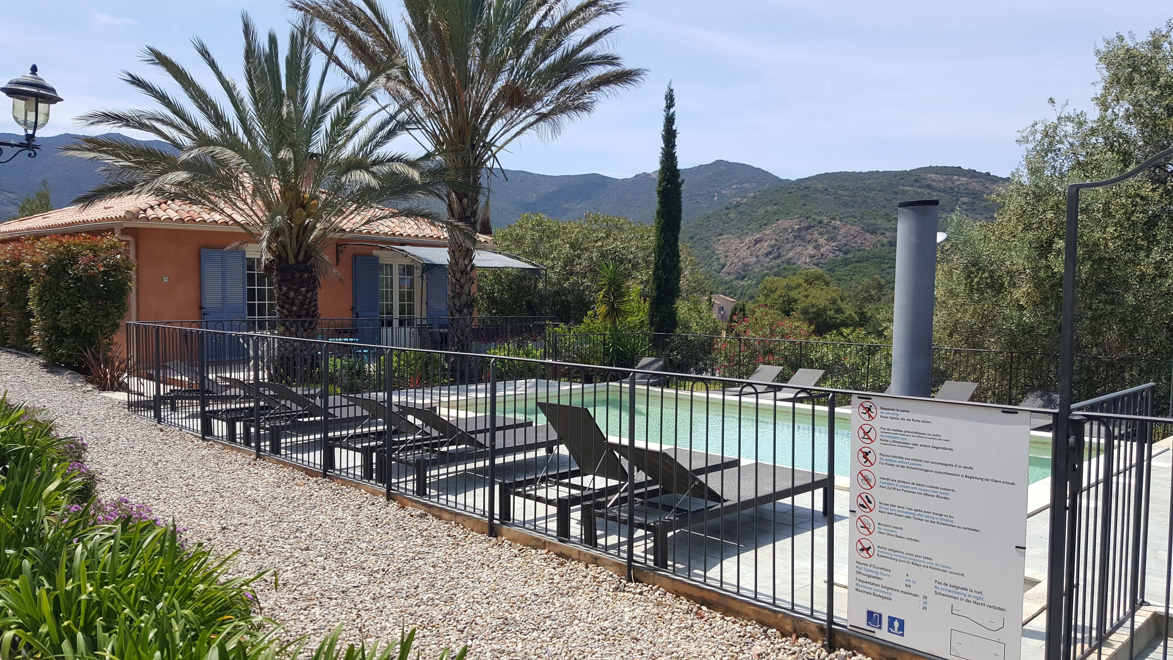 Un espace piscine équipé de chaises longues, entouré d’une clôture et agrémenté d’un panneau indiquant les règles à respecter.
