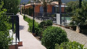A pathway leading to a building with a mountain backdrop, surrounded by greenery and a clear sky. - Villa Primavera (Galeria)