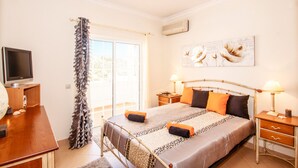 A bedroom with a bed, bedside tables, a television, and a window with curtains.