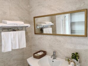 A bathroom with a marble wall, a white sink, a gold-framed mirror, and a towel rack with folded towels. - Artvilla Village (Xihu)