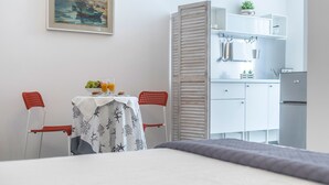 Habitación de hotel con cama, mesa de comedor con desayuno, kitchenette y un cuadro en la pared.
