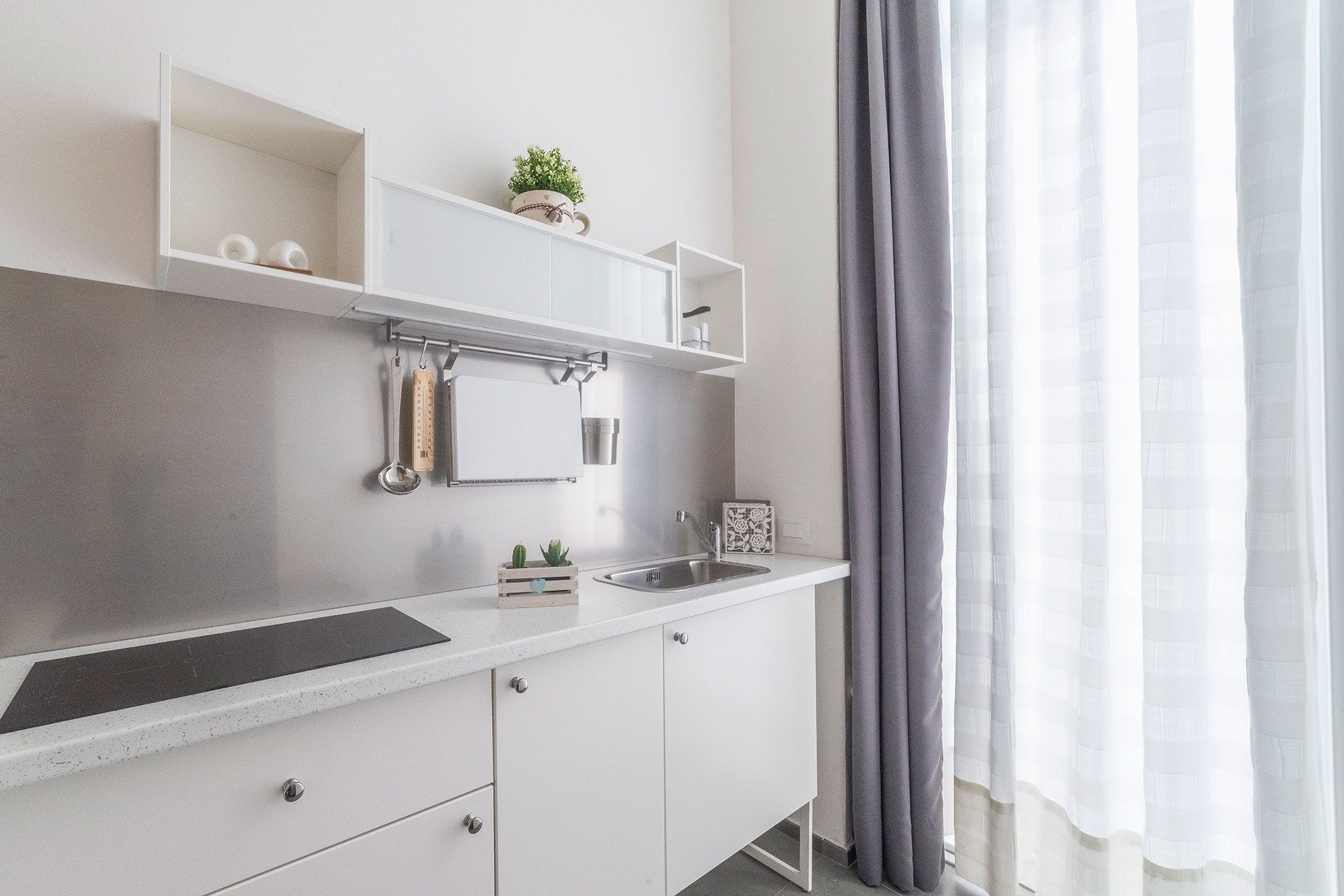 Una cocina moderna con armarios blancos, un lavamanos de acero inoxidable y una pequeña encimera.