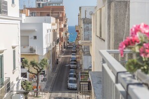 Una calle estrecha bordeada de edificios de varios pisos, con una vista despejada del mar en la distancia y coches aparcados a lo largo de la calzada.
