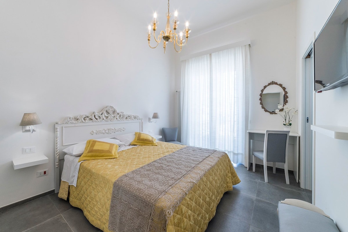 Un dormitorio ordenado con cama, lámparas de noche, un escritorio y un espejo.