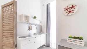 Una cocina moderna con armarios blancos, horno empotrado y encimera gris. Hay una pequeña planta en la encimera y una cortina gris en la ventana.