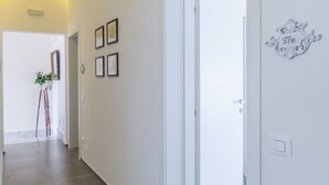 Un pasillo con una puerta blanca, obras de arte enmarcadas en la pared y una planta pequeña.