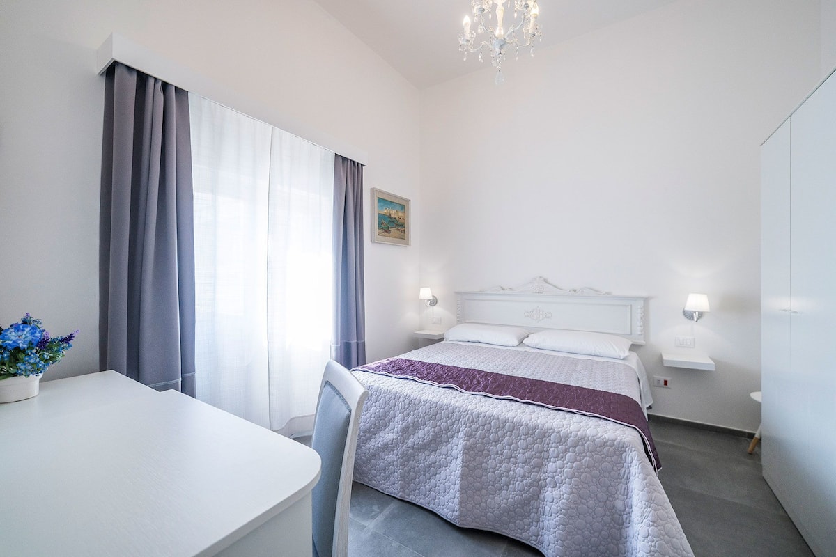 Una habitación de hotel con cama, lámparas de noche, escritorio y una silla.