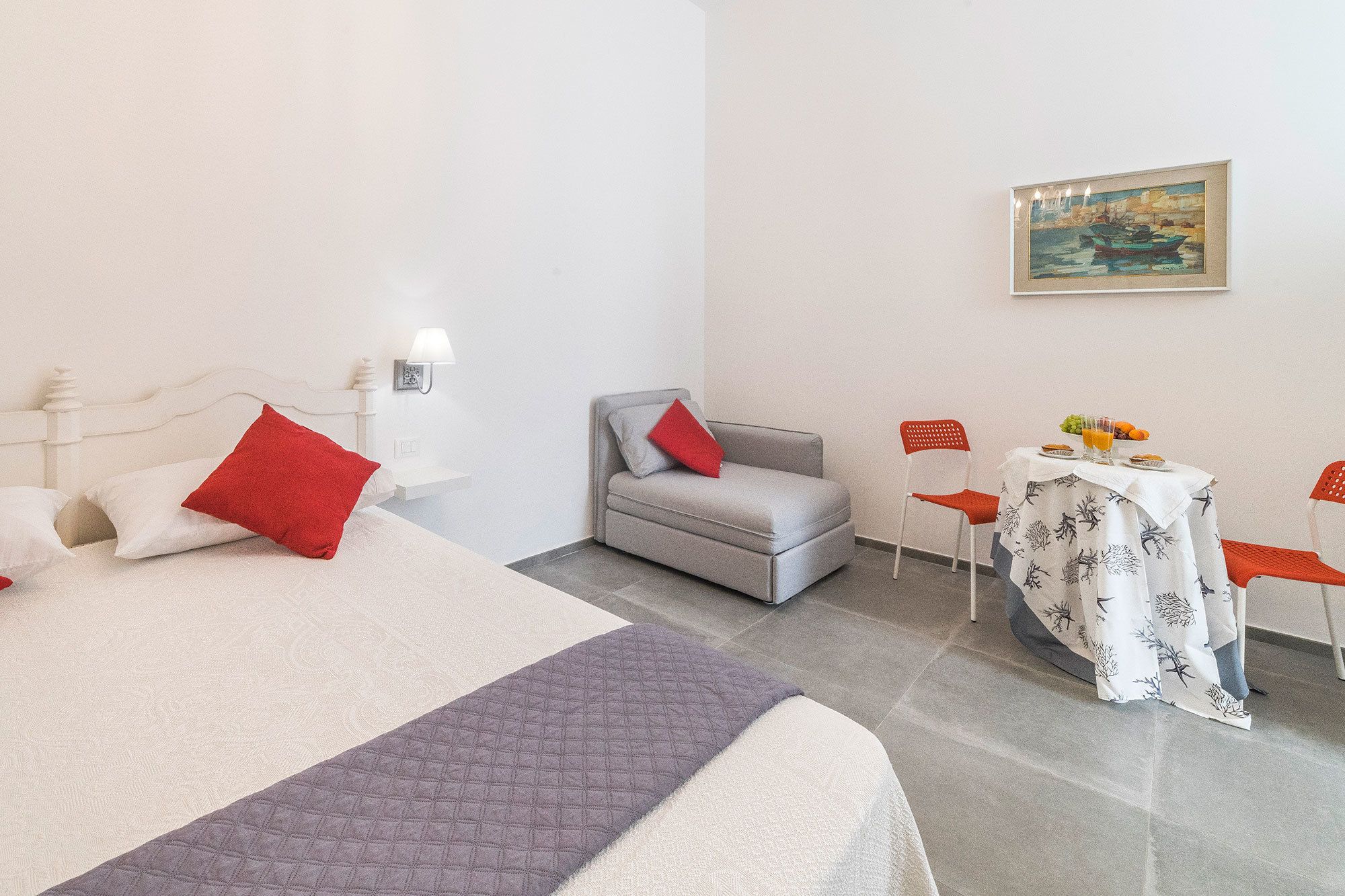 Ein Hotelzimmer mit einem Bett, einem grauen Sofa, einem kleinen Tisch mit Tischdecke und einem Bild an der Wand.