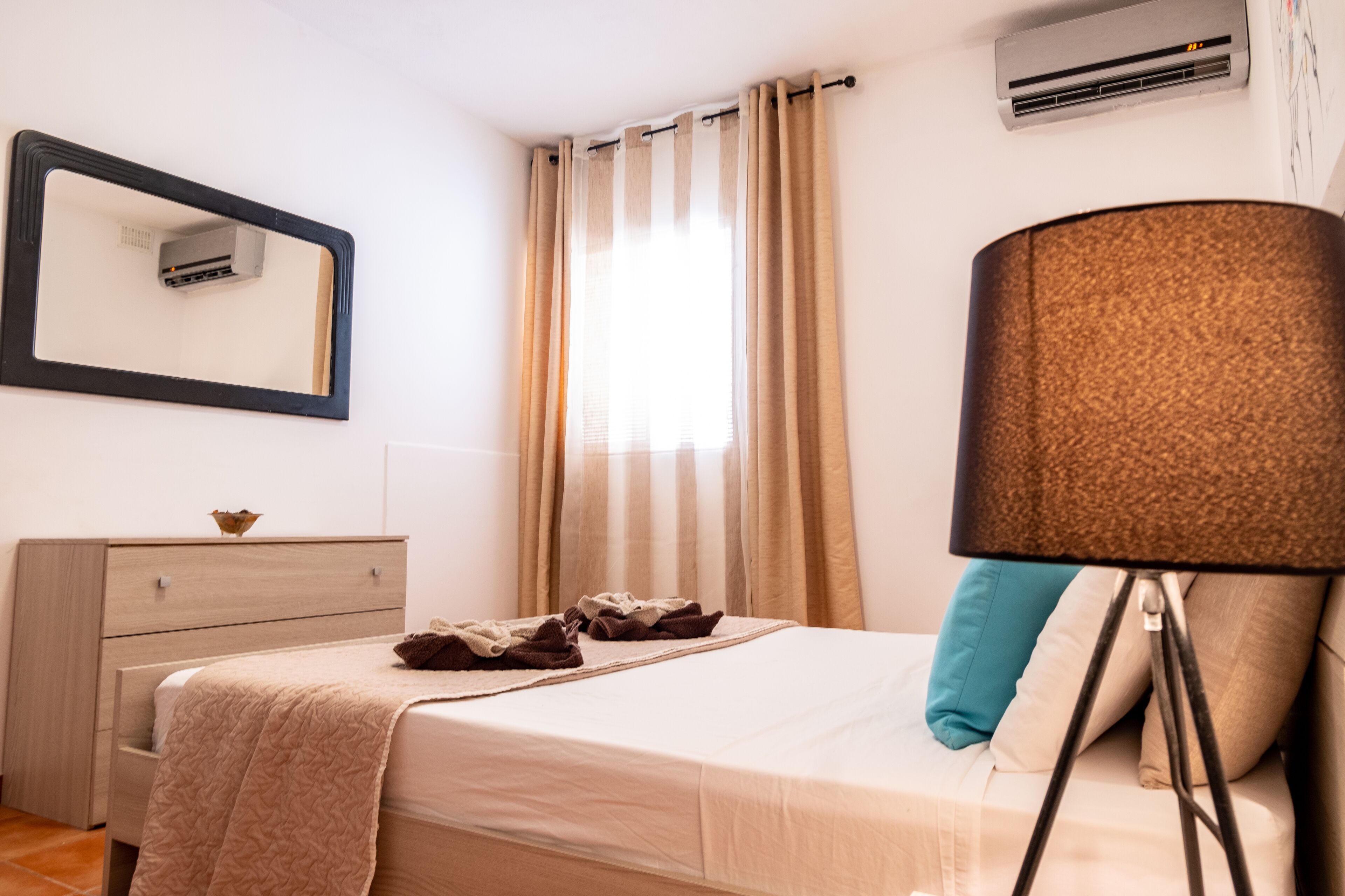 Una camera da letto ordinata con un letto, una cassettiera, uno specchio e una lampada.