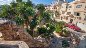 A residential area with stone walls, palm trees, and a red car parked on the street. - D View 4 You (Mellieha)