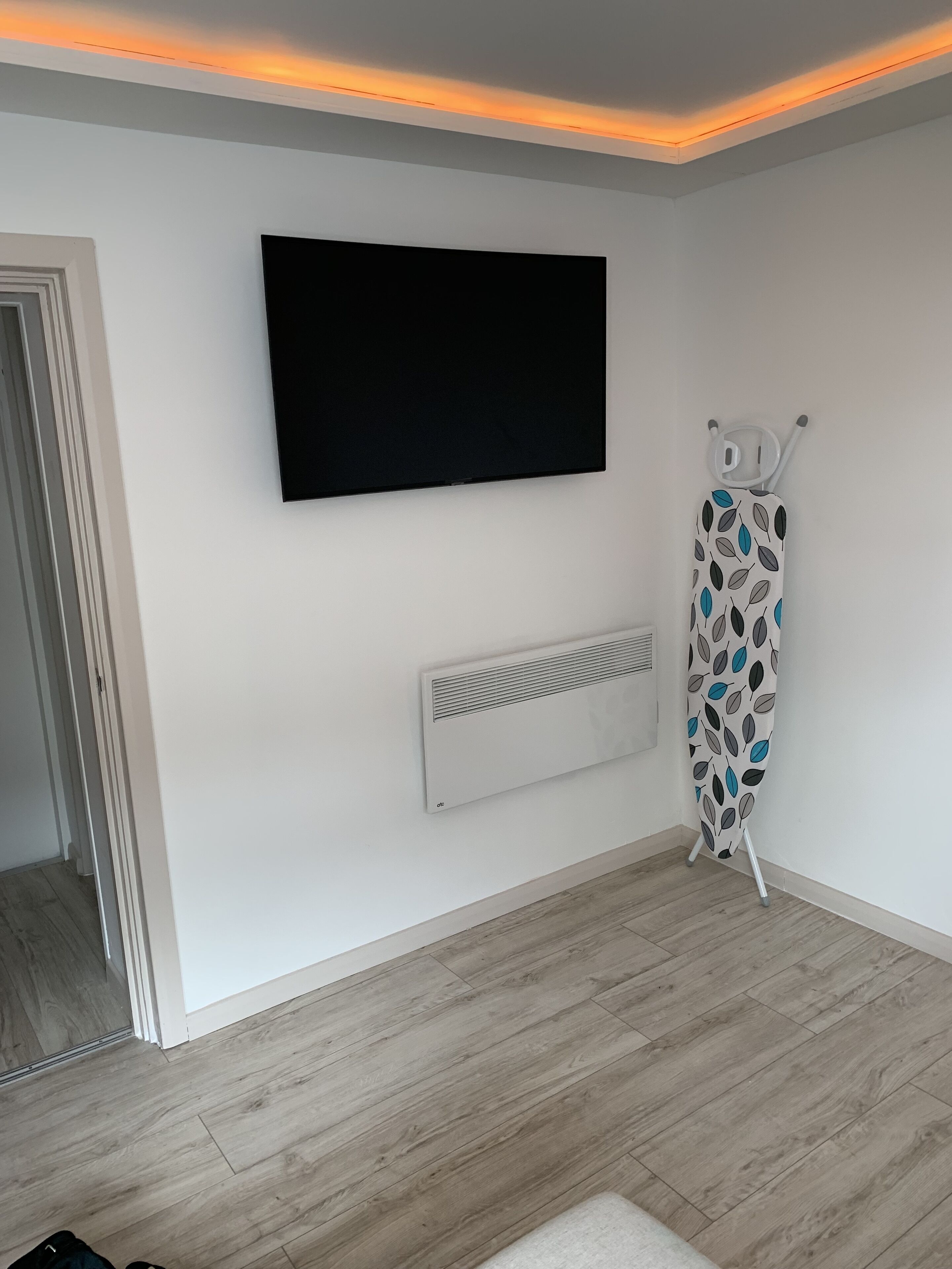 A room with a mounted TV, a radiator, and a patterned ironing board.