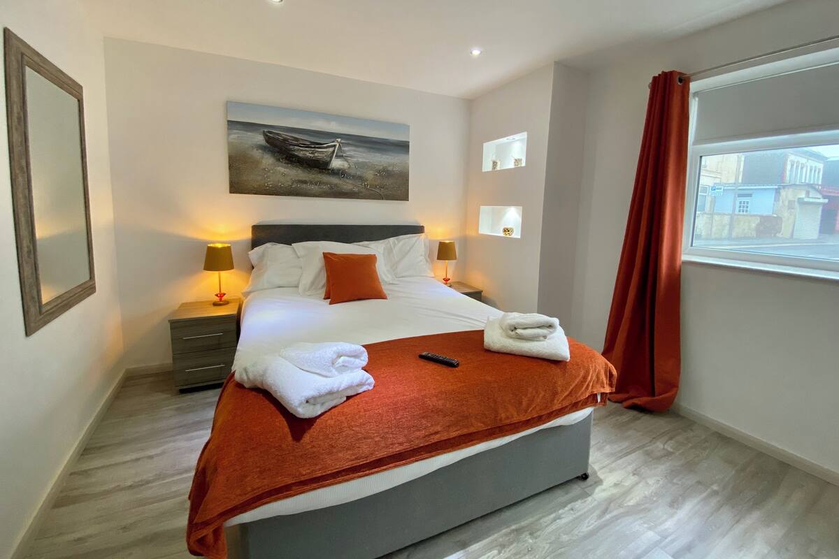 A modern hotel room with a large bed, a painting on the wall, and a view of the city through the window.