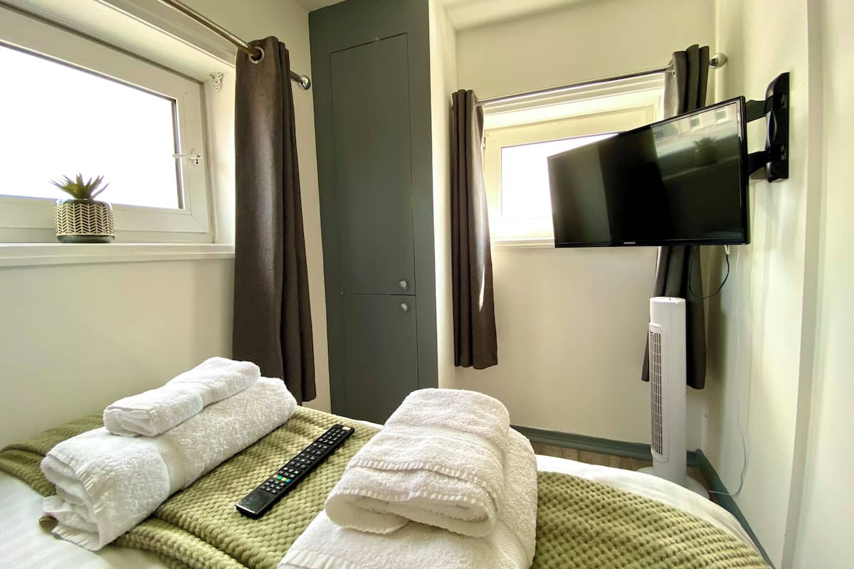 A hotel room with a bed, a remote control, a television, and a window with curtains.