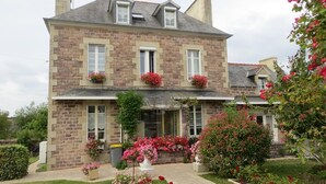 A two-story stone building with a central entrance, flower boxes on the windows, and a well-maintained garden with various plants and flowers. - Maison du Carrec (Paimpol)