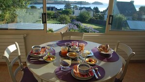 A breakfast table set with various dishes and drinks, overlooking a scenic view of a lake and houses. - Maison du Carrec (Paimpol)