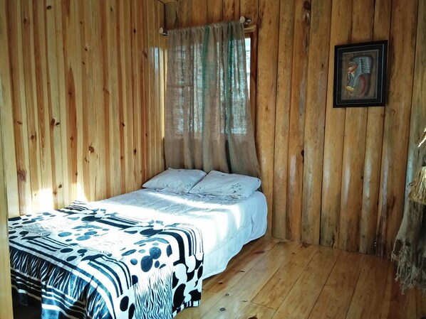 A wooden room with a bed, a window with curtains, and a framed picture on the wall. - Agape Log Cabin and Restaurant (Sagada)