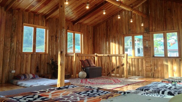 Une cabane en bois rustique avec un plafond haut, de grandes fenêtres et un intérieur chaleureux comprenant un lit, des oreillers et un tapis.