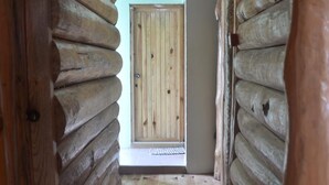 L’intérieur d’une cabane en rondins, avec un plancher en bois, un tapis à motifs et une porte donnant sur une pièce offrant une vue panoramique.