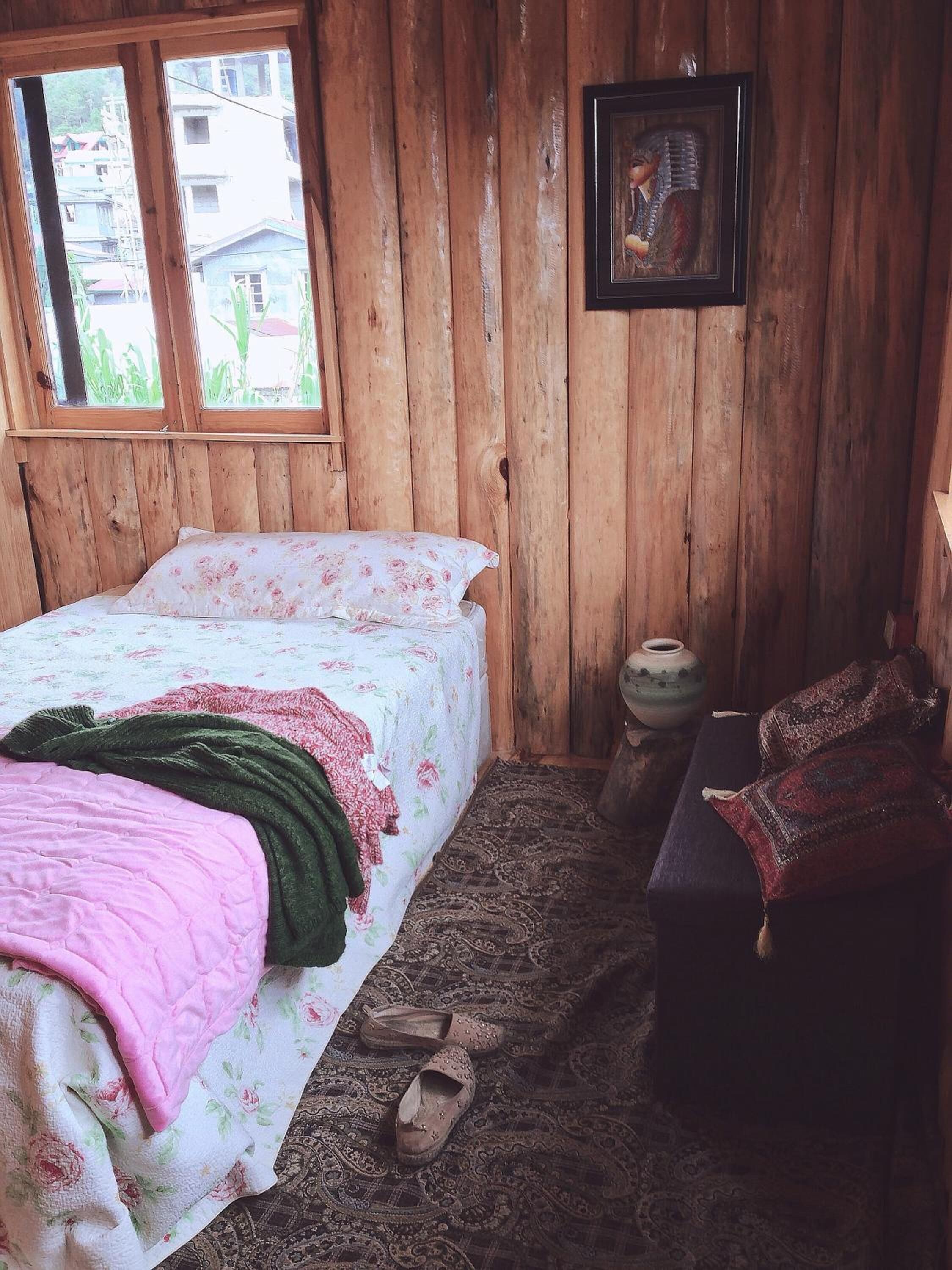 A wooden room with a bed, a small table, and a window.