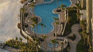 A pool area with multiple swimming pools, palm trees, and lounge chairs. - Clam Shell at Grand Panama - Intimate and Serene Perfect spot for relaxing (Panama City Beach)
