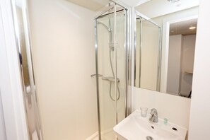 A bathroom with a glass-enclosed shower, a white sink, and a mirror. - Axo Paradise village (Coventry)