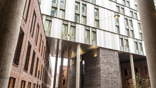 A modern building with a courtyard, featuring a mix of brick and glass facades, large columns, and a paved walkway. - Axo Paradise village (Coventry)
