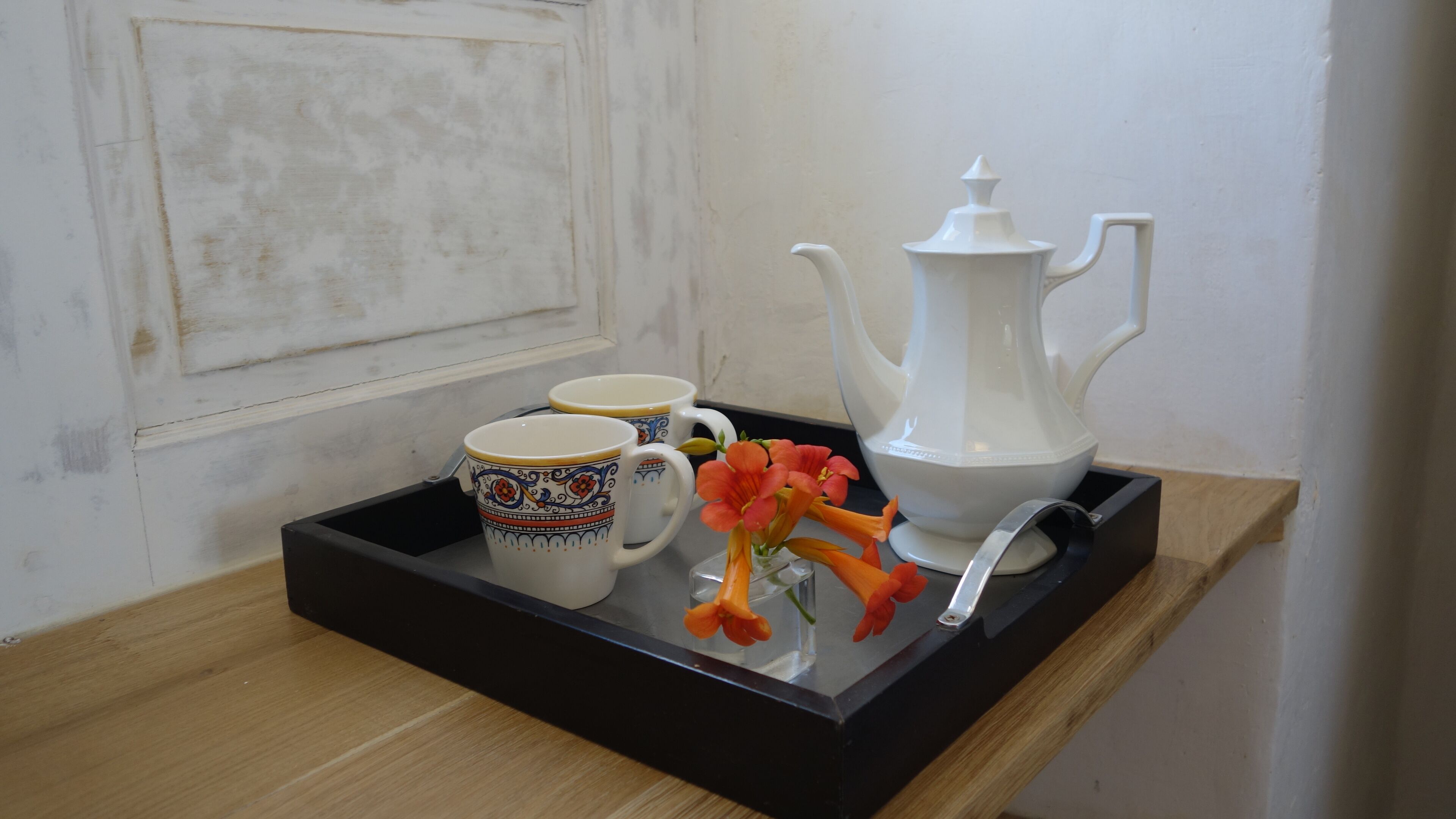 A tray with a white teapot, two patterned cups, and orange flowers on a wooden surface.