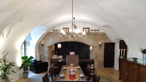 Uma sala de jantar com uma mesa comprida, cadeiras, um candelabro e uma lareira de pedra.