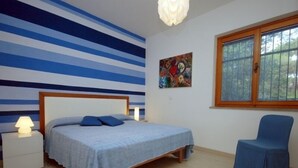 Ein Schlafzimmer mit einem Bett, einem Sessel, einem Nachttisch, einem Gemälde und einem Fenster.