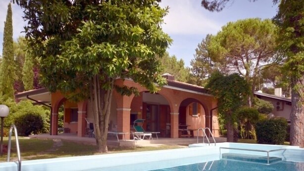 Ein Swimmingpool mit klarer, blauer Wasseroberfläche, umgeben von einem Ziegelgebäude mit Bogenfenstern und einer überdachten Terrasse.