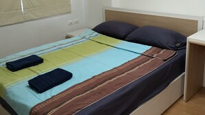 A bed with a striped bedspread and two pillows, a bedside table, and an air conditioning unit on the wall. - Comfy Deluxe One Bedroom (Bangkok)