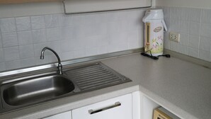 A kitchen with a stainless steel sink, a microwave, and a white cabinet with a handle. - Comfy Deluxe One Bedroom (Bangkok)