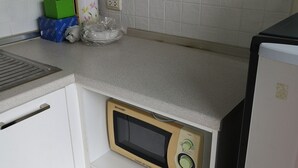 A compact kitchen with white cabinets, a microwave oven, and a refrigerator. - Comfy Deluxe One Bedroom (Bangkok)