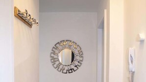 Un pasillo estrecho con un espejo decorativo en la pared, un teléfono y una puerta a la izquierda.