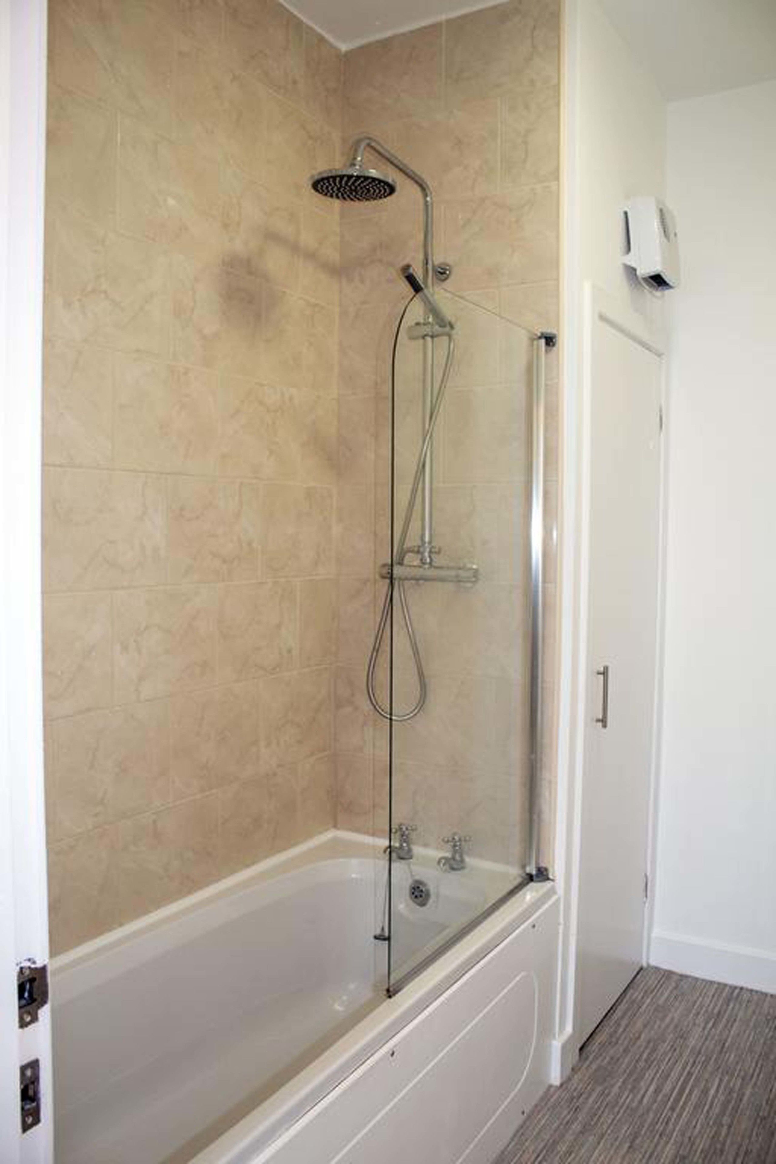 Une salle de bain avec une douche à parois de verre, une baignoire et des murs recouverts de carreaux beiges.