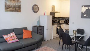 Un espacio habitable compacto con sofá, una pequeña mesa de comedor y kitchenette.