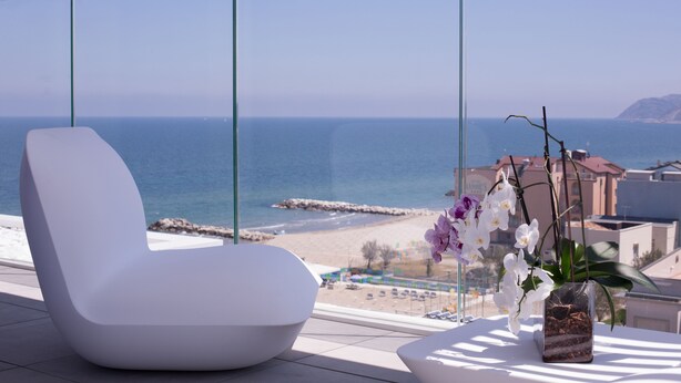 Ein moderner Balkon mit einem weißen Stuhl, einer Orchideen-Vase und Blick auf das Meer und den Strand.